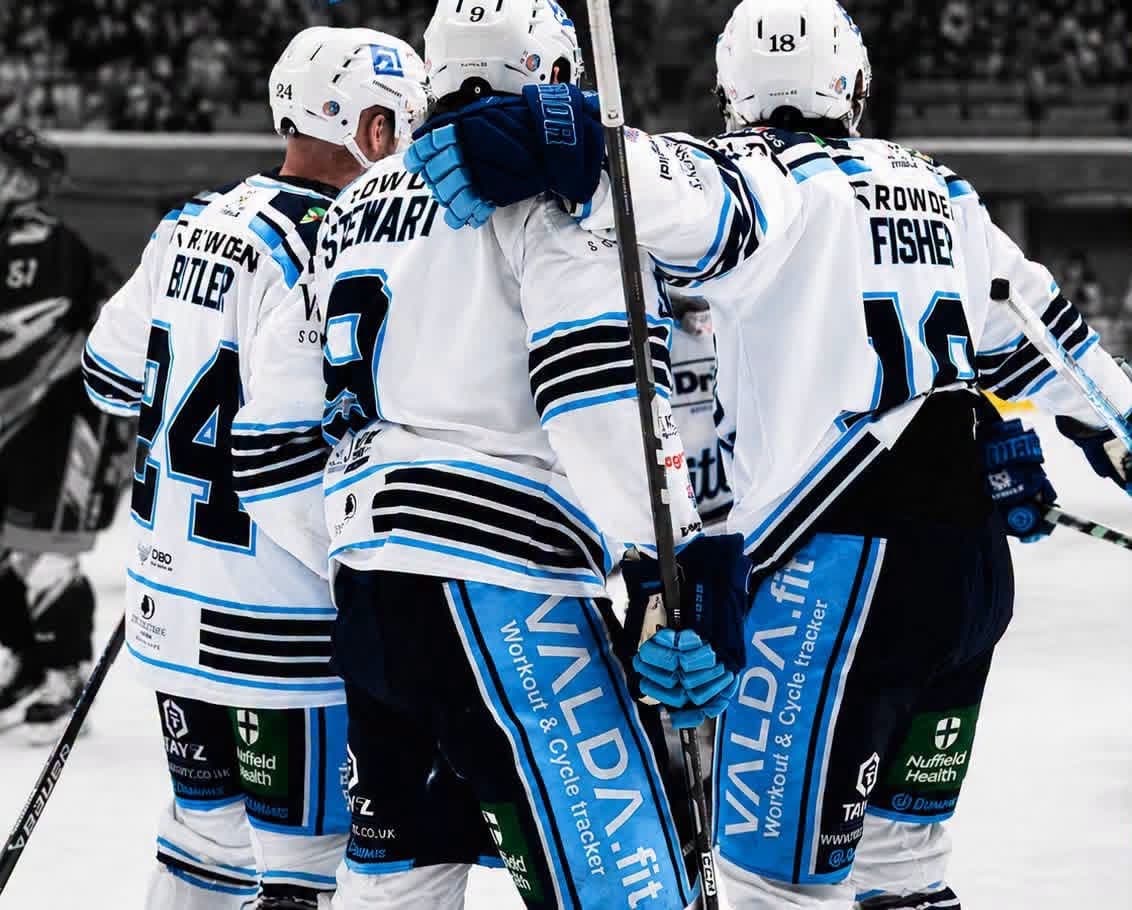 Three Bristol Pitbulls players in white kit embrace on the ice, seen from behind, with VALDA.fit on their shorts